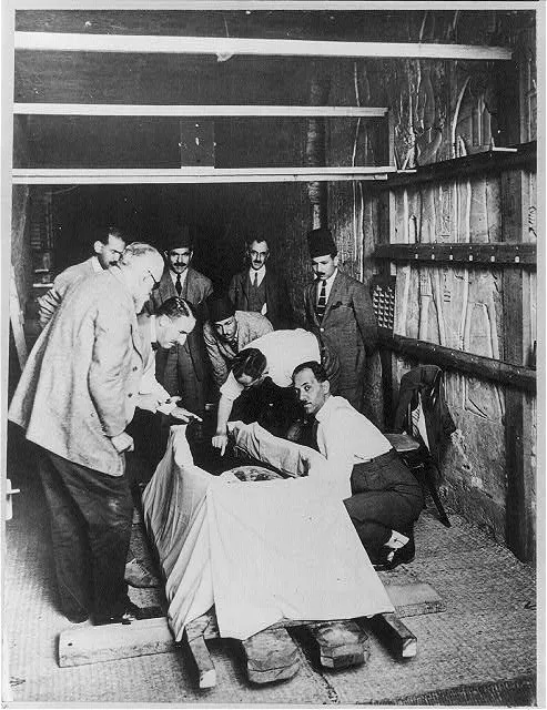 [Howard Carter, 1873-1939, with magnifying glass, leaning over mummy of King Tutankhamen as the first incision was made in the mummy wrappings, Feb. 1926]
