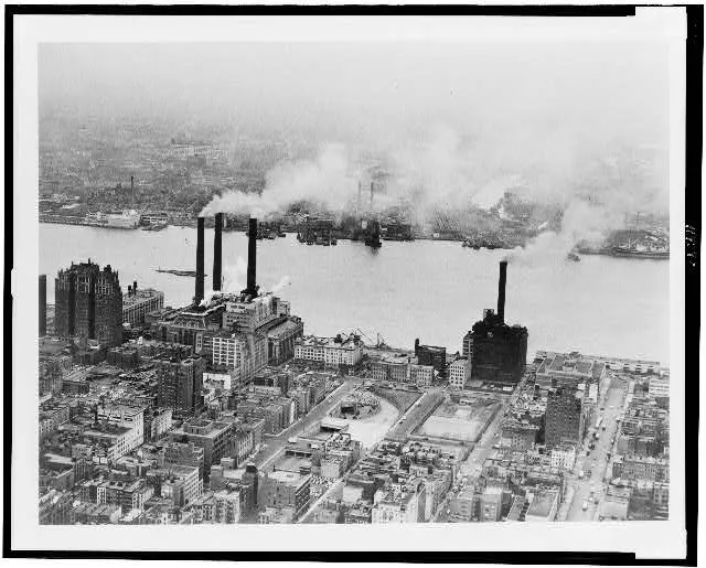 [Smoke issues from stacks of industrial buildings along river]