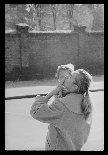 [Woman holding a child and gesturing near the Berlin Wall in West Berlin, looking towards East Berlin]