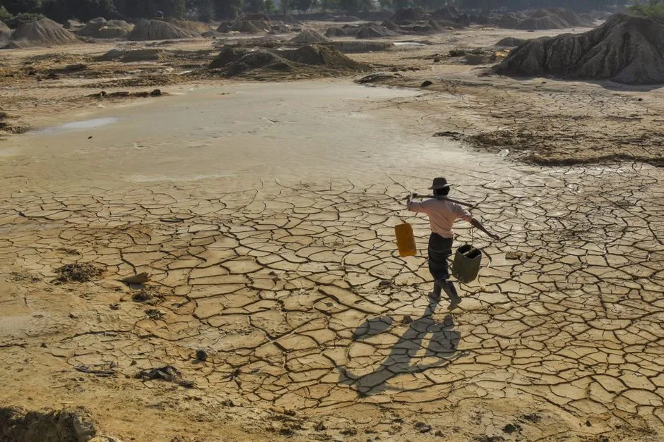 A man carries water across a parched landscape in Sagaing, revealing drought impact.
