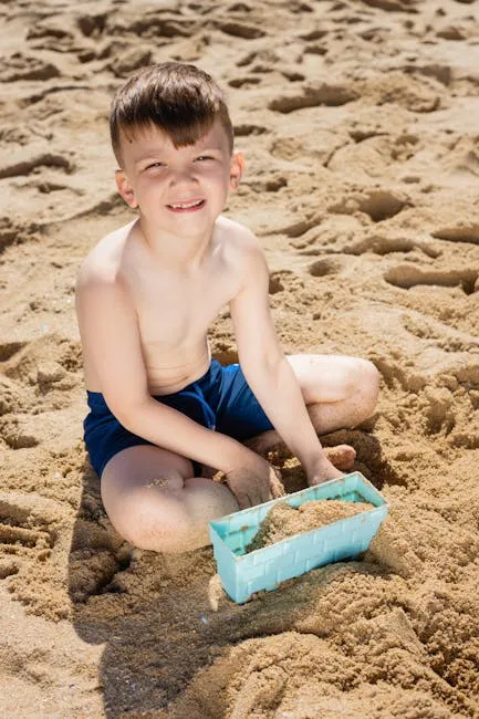 A young boy enjoys a sunny day playing with sand on the beach, smiling brightly.