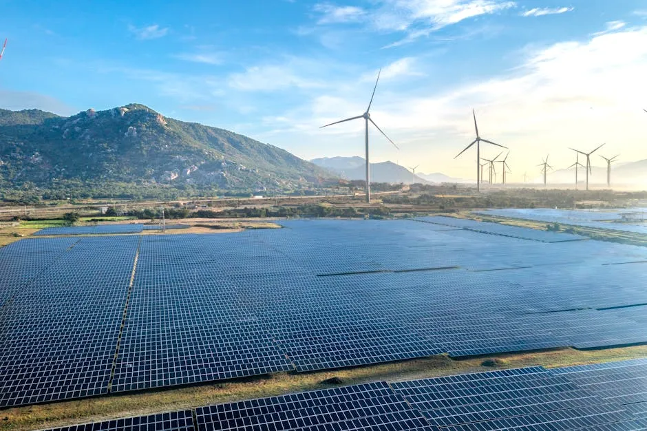 A field of solar panels with wind turbines under a sky.