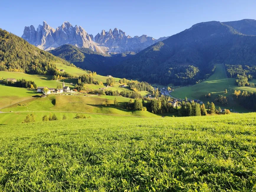 Breathtaking landscape of the Dolomites, lush valleys, and rural houses under a clear blue sky.