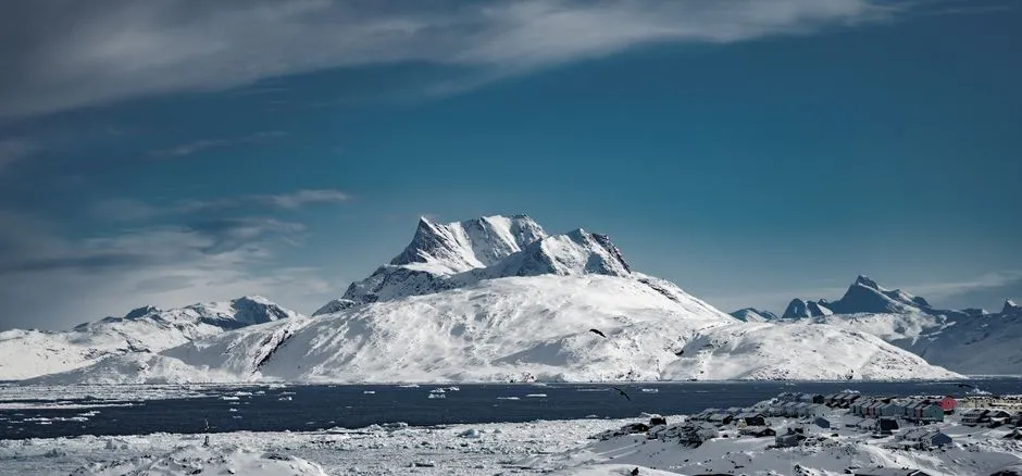 Breathtaking view of snowy mountains in Nuuk, Greenland surrounded by icy waters and clear blue skies.