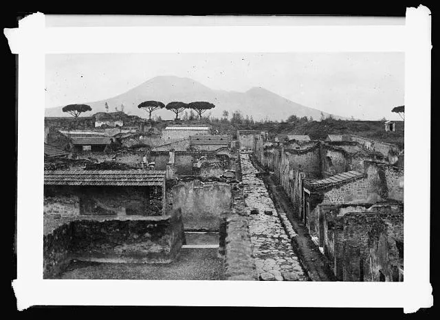 Building Methods in Christ's Time. A view of the resurrected city of Pompeii, showing the solid construction methods used in building the homes of those ancient times. Note the remnants of slate roof construction, which shows very little difference from the methods employed today. Distributing relief in this district, American Red Cross workers have found several families who have taken refuge in the ruins of this centuries old city. Some of them have made themselves quite comfortable under the shelter of roofs and walls that were buried for a thousand years. In the background can be seen Mt. Vesuvius the eruption of which buried Pompeii in volcanic ash