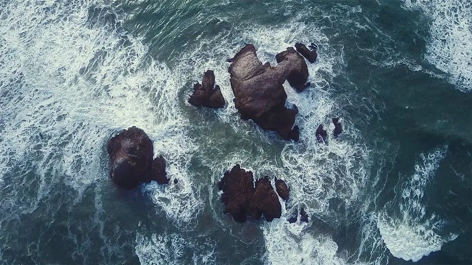 Dynamic aerial view of ocean waves crashing against rocky structures, captured from above.