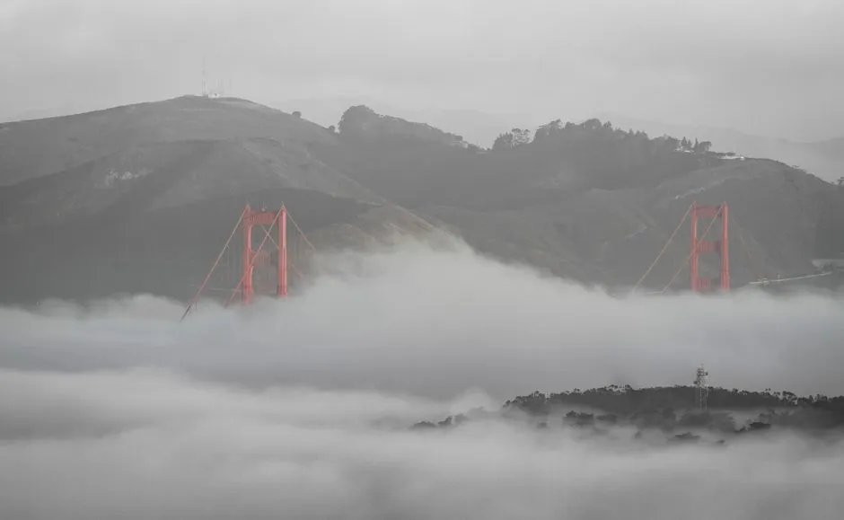 Golden Gate Bridge emerging from fog with hills in the background, capturing a moody San Francisco scene.