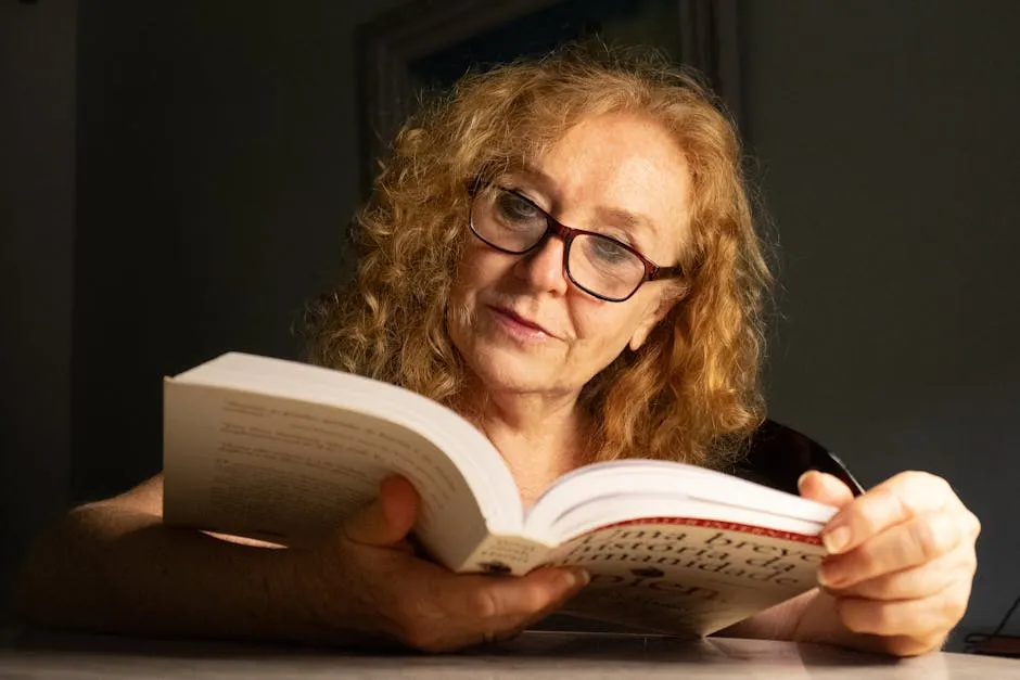 Senior woman with glasses reading a book in a cozy indoor setting, focused and relaxed.