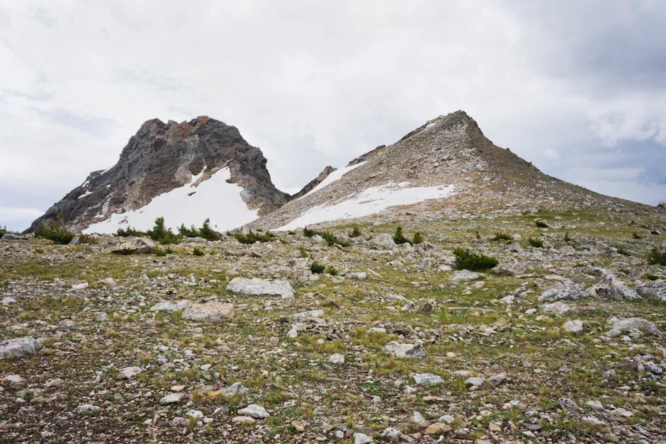 Stunning view of rocky mountains with patches of snow under a cloudy sky.