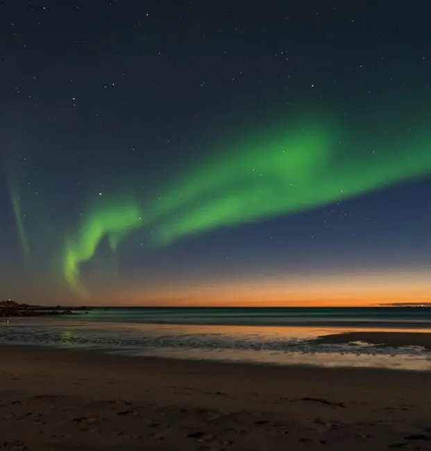 Stunning view of the aurora borealis dancing over a tranquil beach in Nordland, Norway at twilight.