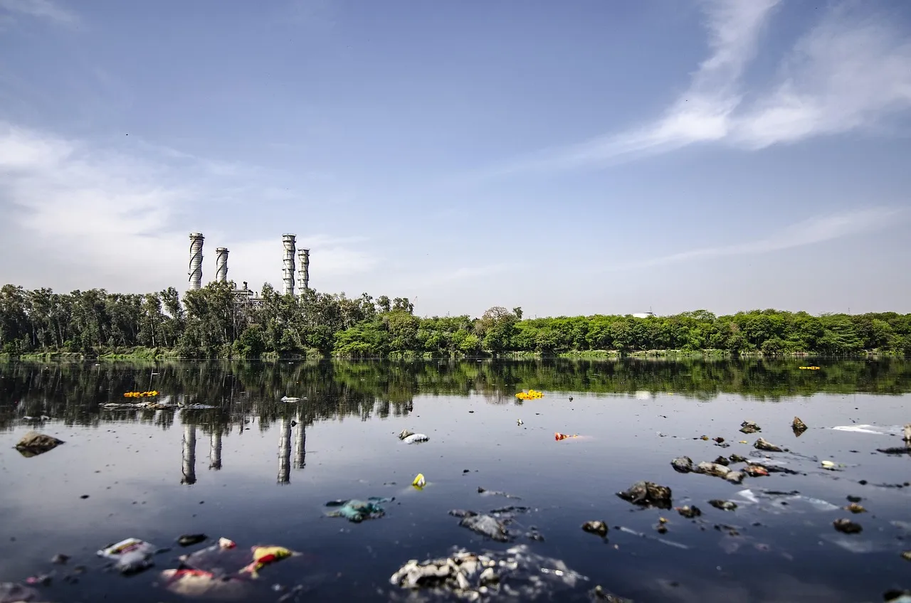 Floating plastic waste in dark water with industrial chimneys in background.